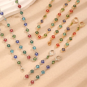 Flat lay of colorful four-leaf clover necklaces and bracelets on textured beige surface