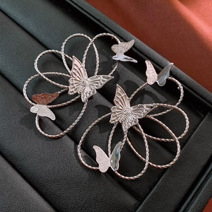 Close-up of silver butterfly earrings with hollow metal coils on black leather stand