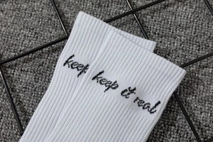 Detail of white cotton ribbed crew socks featuring black keep it real embroidery
