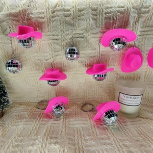 Pink cowgirl hat and disco ball earrings with matching keychains on a woven surface
