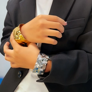 Detail of wide irregular wave texture bangles in gold and silver finish on a model