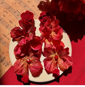 Detail shot of red rose earrings with fabric texture on a decorative vintage score