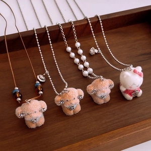Detail of plush puppy and kitty pendants on pearl and silver chains with saturn logo