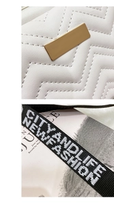 Detail of white quilted camera bag featuring golden metal clasp and black lettered wide strap