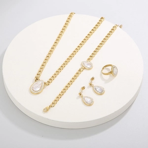Detailed set of gold teardrop jewelry with white shell and crystals on display stand