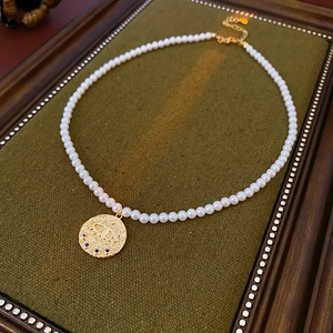 Détail du pendentif œil plaqué or serti de zircons colorés sur un collier de perles