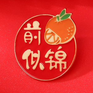 Red enamel brooch with orange pattern and gold text symbolising success and good luck