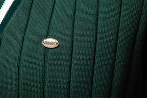 Dettaglio del cardigan a coste verde scuro con placca logo dorata e trama in maglia spessa