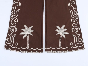 Detail of dark brown trousers with white palm tree embroidery and wavy hem design