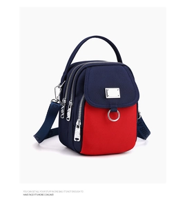 Detail view of multi-compartment navy and red nylon crossbody bag with zipper closures