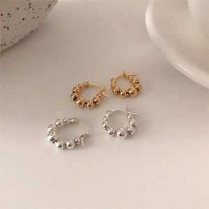 Close-up of gold and silver S925 sterling silver beaded hoop earrings on a light surface
