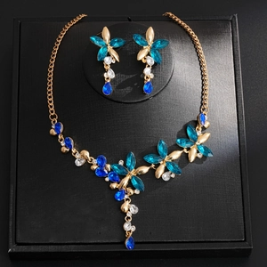 Elegant gold-tone flower jewelry set with blue crystals on black display stand