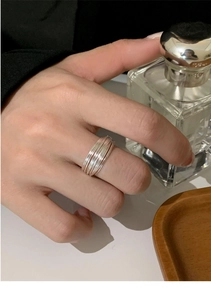 Macro detail of layered minimalist silver rings styled on a finger with perfume