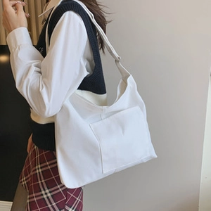 Side view of a large white canvas tote bag with an outer pocket on a female model