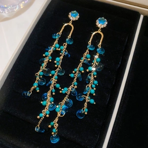 Detail view of long tassel earrings with green stones and sparkling crystals on black velvet