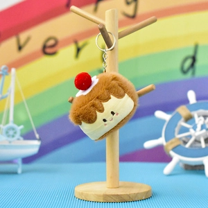 Detailed shot of a cute plush croissant cake keychain with red cherry on a wooden display stand