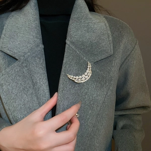 Macro view of a 18k gold crescent brooch with pearls and zircon on a wool coat