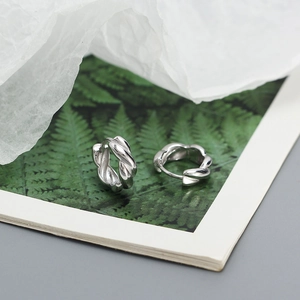 Detailed close-up of twisted silver S925 hoop earrings on a minimalist natural background