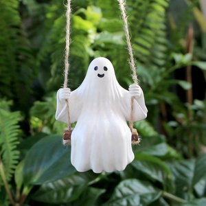 Detailed close-up of a white ghost figurine sitting on a small wooden swing in a garden