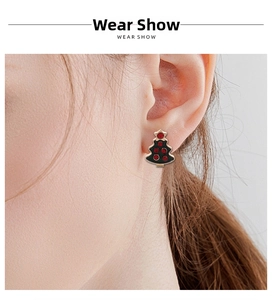 Close-up of a Christmas tree stud earring with black enamel and red rhinestones on an ear