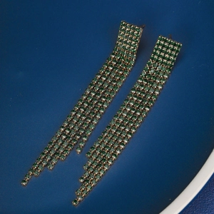Detail of long tassel earrings featuring emerald green rhinestones and a golden finish