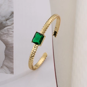 Detailed close-up of gold-plated cuff featuring an emerald-cut green gemstone and textured band