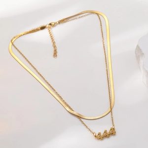 Double-layered gold stainless steel necklace with 444 angel number pendant on a white rock