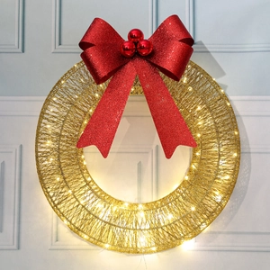 Detail of Christmas wreath with red glitter bow and warm LED lights on white wood background