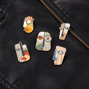 Detailed view of five abstract face enamel pins on black leather jacket with metal zippers