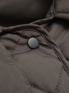 Macro shot of olive quilted jacket fabric with matte black button and fine stitching