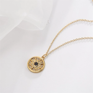 Close-up of a golden sunburst pendant necklace with a blue gemstone on white fabric