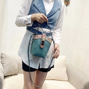Detail view of teal bucket bag with floral embroidery and gold chain strap held by model