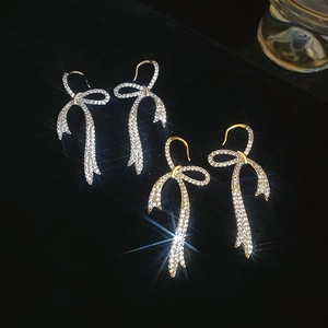 Macro shot of gold and silver bow drop earrings with sparkling zircon on dark velvet