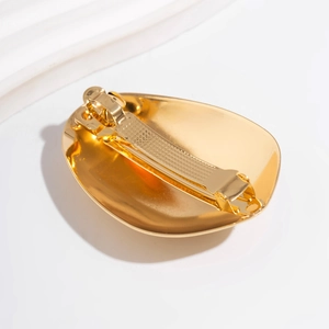 Detail of the golden oval hair clip showing back spring barrette and anti-slip texture