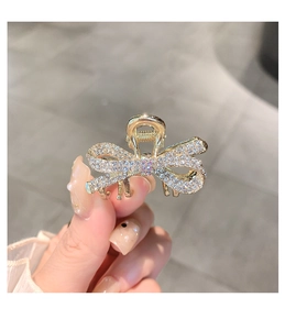 Close-up of a small golden bow hair claw clip with rhinestones held in hand