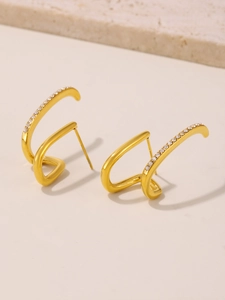 Detail of gold curved earrings with sparkling cubic zirconia on a marble surface