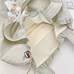Detail view of the embroidered canvas tote bag with internal zipper pocket and drawstring closure