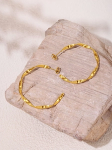 Close-up of gold-plated twisted hoop earrings on a natural stone with soft shadows