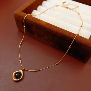 Detail of gold beaded chain necklace featuring a polished black stone drop pendant