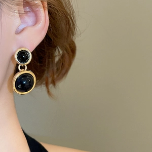 Detail of elegant gold-framed black resin double-tier earrings worn by a model