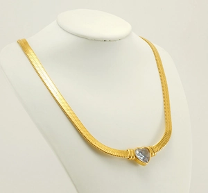 Detail showing gold snake chain with heart zircon pendant on white jewelry display stand