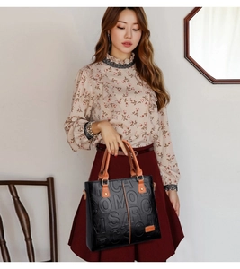 Detail of embossed texture and brown handles on a black high-capacity tote shoulder bag