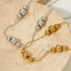 Polished gold and silver ball pendant necklaces on marble tray for a modern style
