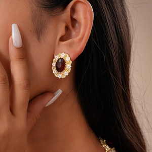 Macro view of vintage gold flower earrings with red oval gemstone on model