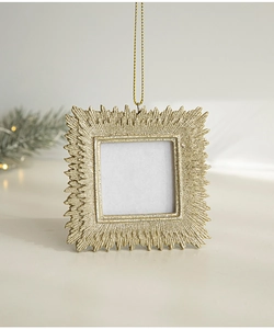 Close-up of golden square photo frame ornament with textured sunburst pattern and gold string