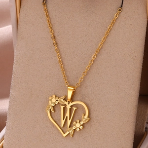 Dettaglio del ciondolo a cuore dorato con lettera W e decorazioni floreali su supporto per gioielli