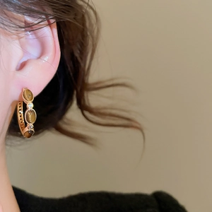 Close-up of gold plated tiger eye hoop earrings with sparkling zircon on ear model