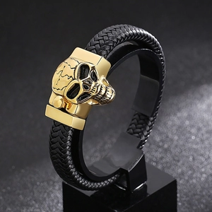 Close-up of black braided leather bracelet with a gold skull clasp on a dark display stand
