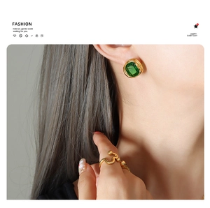 Close-up of emerald square earrings and wavy gold ring worn by a fashion model