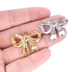 Close-up of gold and silver bow pendants held in hand showing fine metal texture